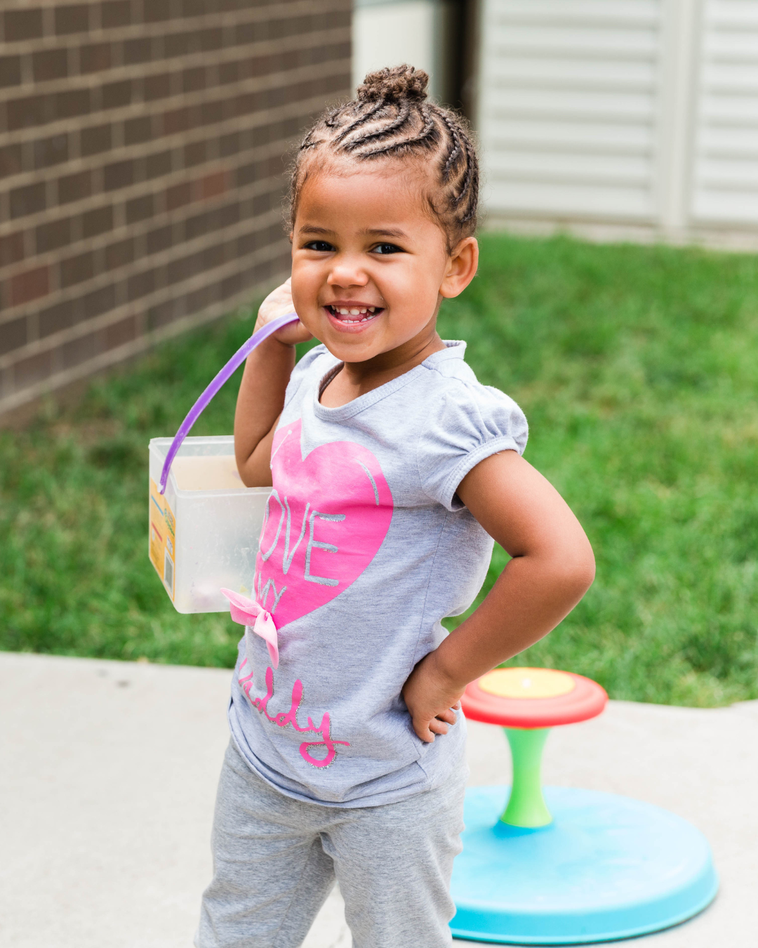 photo of a smiling girl carrying chalk on playground striking a pose for the camera